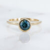 ava-teal-sapphire-round-bezel-set-engagement-ring-with-peak-a-boo-diamond